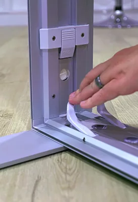 a mans hand closing pressing a clip to snap the base of the lightbox to the feet of the lightbox